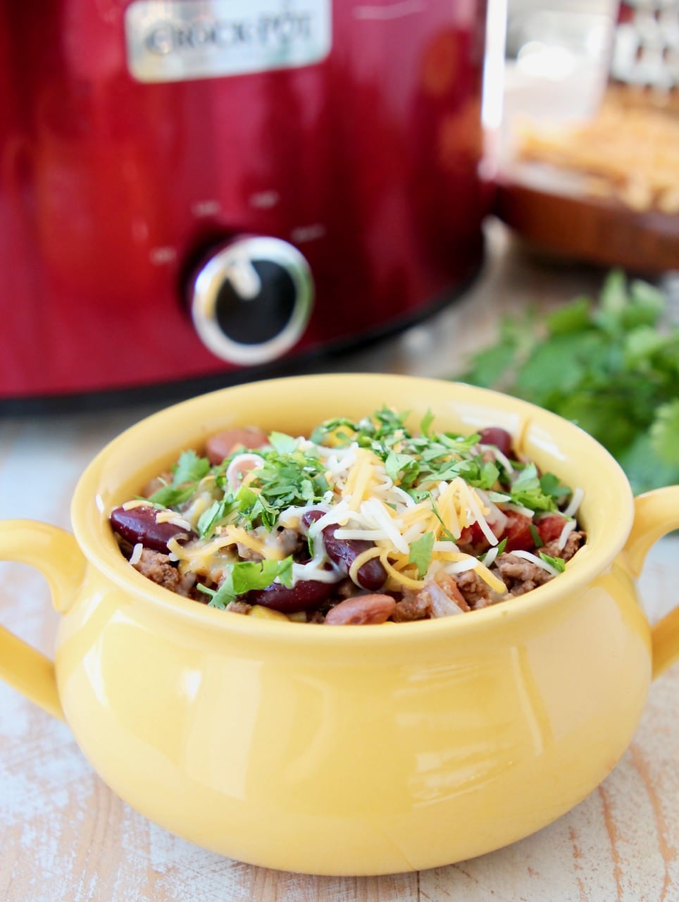 Crockpot taco soup in yellow crock with cheddar cheese and fresh cilantro and red crock pot