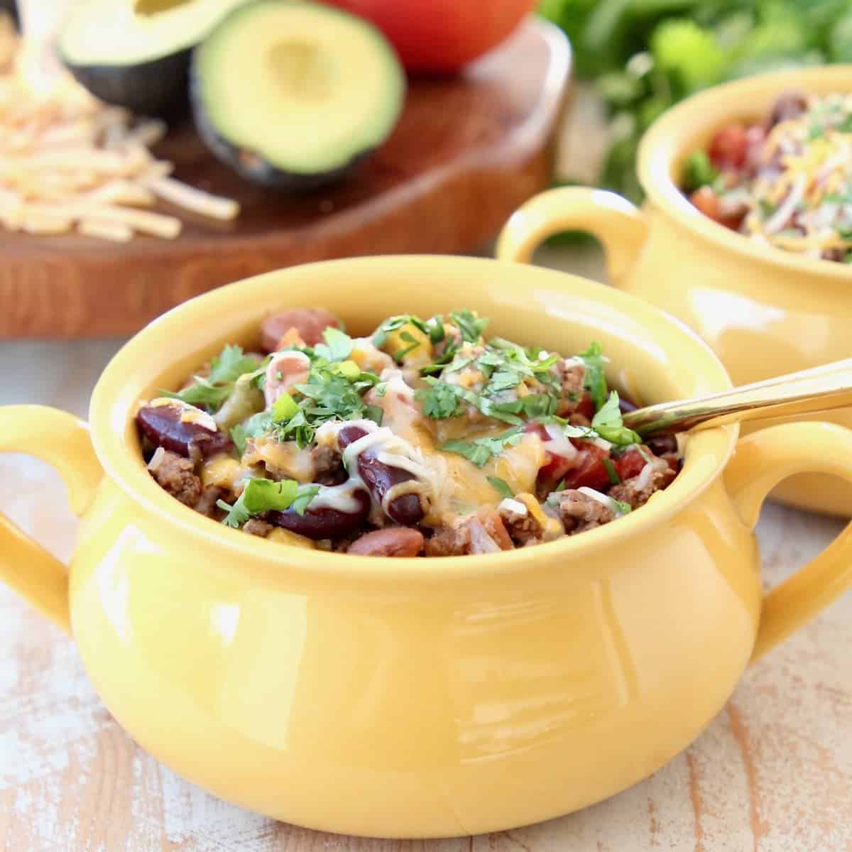 Crockpot Taco Soup in yellow crock with gold spoon, topped with cheddar cheese and fresh cilantro