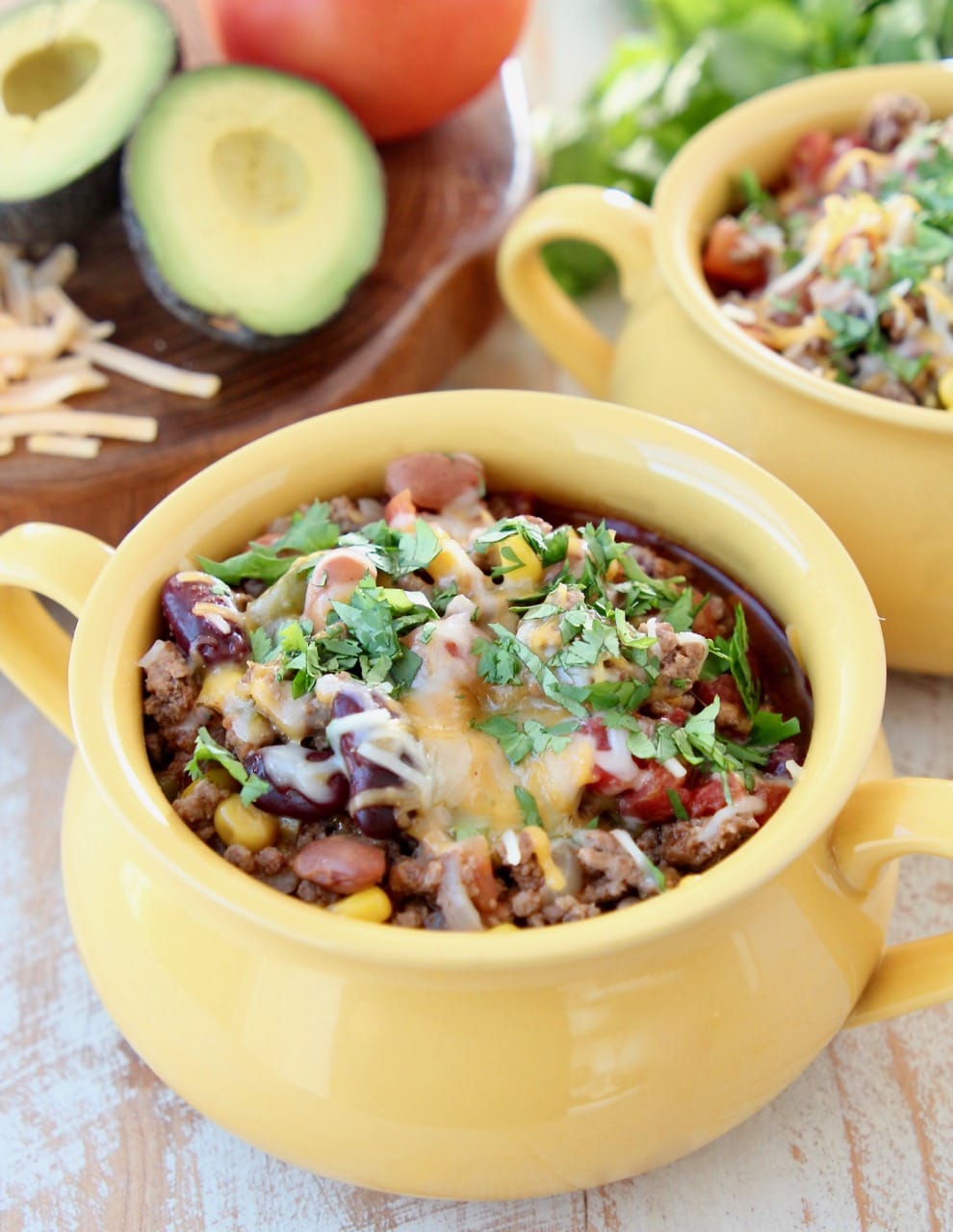 Taco soup in a yellow crock with cheddar cheese and fresh cilantro