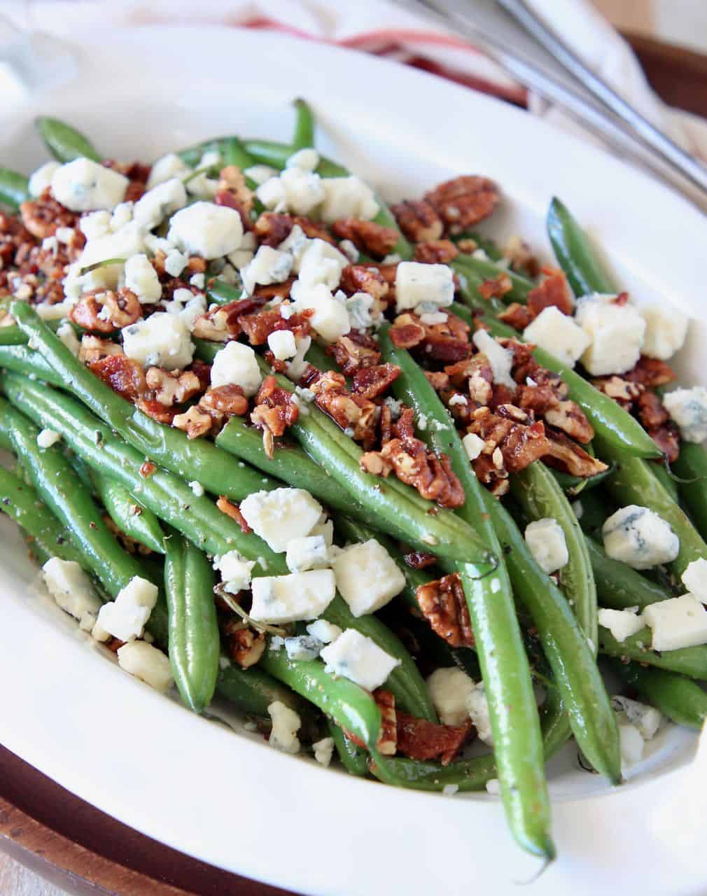 Fresh green beans in serving bowl, topped with pecans and blue cheese crumbles
