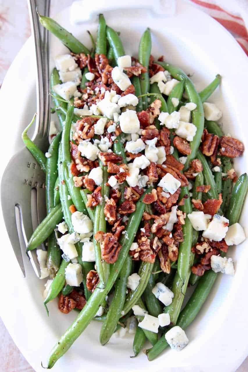 Fresh green beans in bowl topped with bacon crumbles, chopped pecans and blue cheese