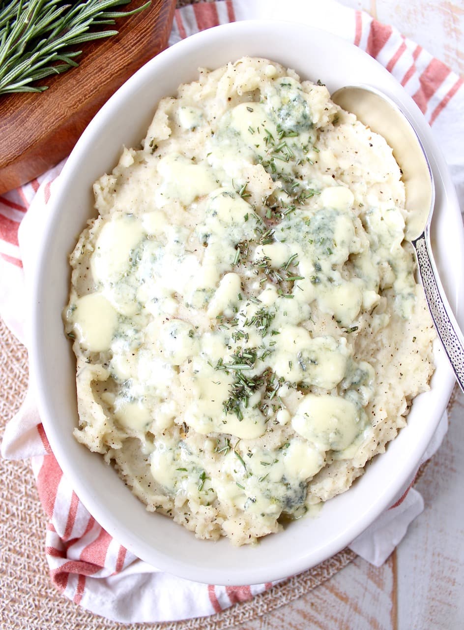 mashed potatoes in bowl topped with blue cheese and fresh chopped rosemary