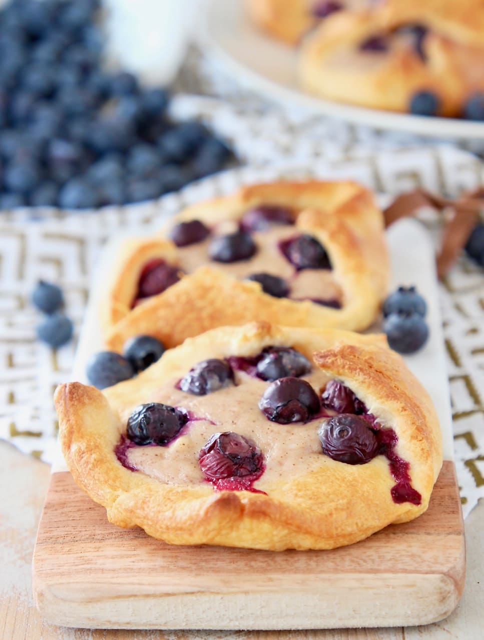 Blueberry pastry made with crescent roll dough, sitting on wood and marble cutting board with fresh blueberries on the side and behind