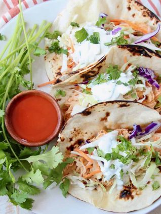 Tacos on plate with small wooden bowl of buffalo sauce on the side