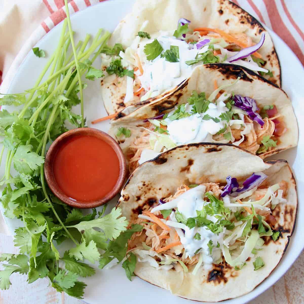 Tacos on plate with small wooden bowl of buffalo sauce on the side