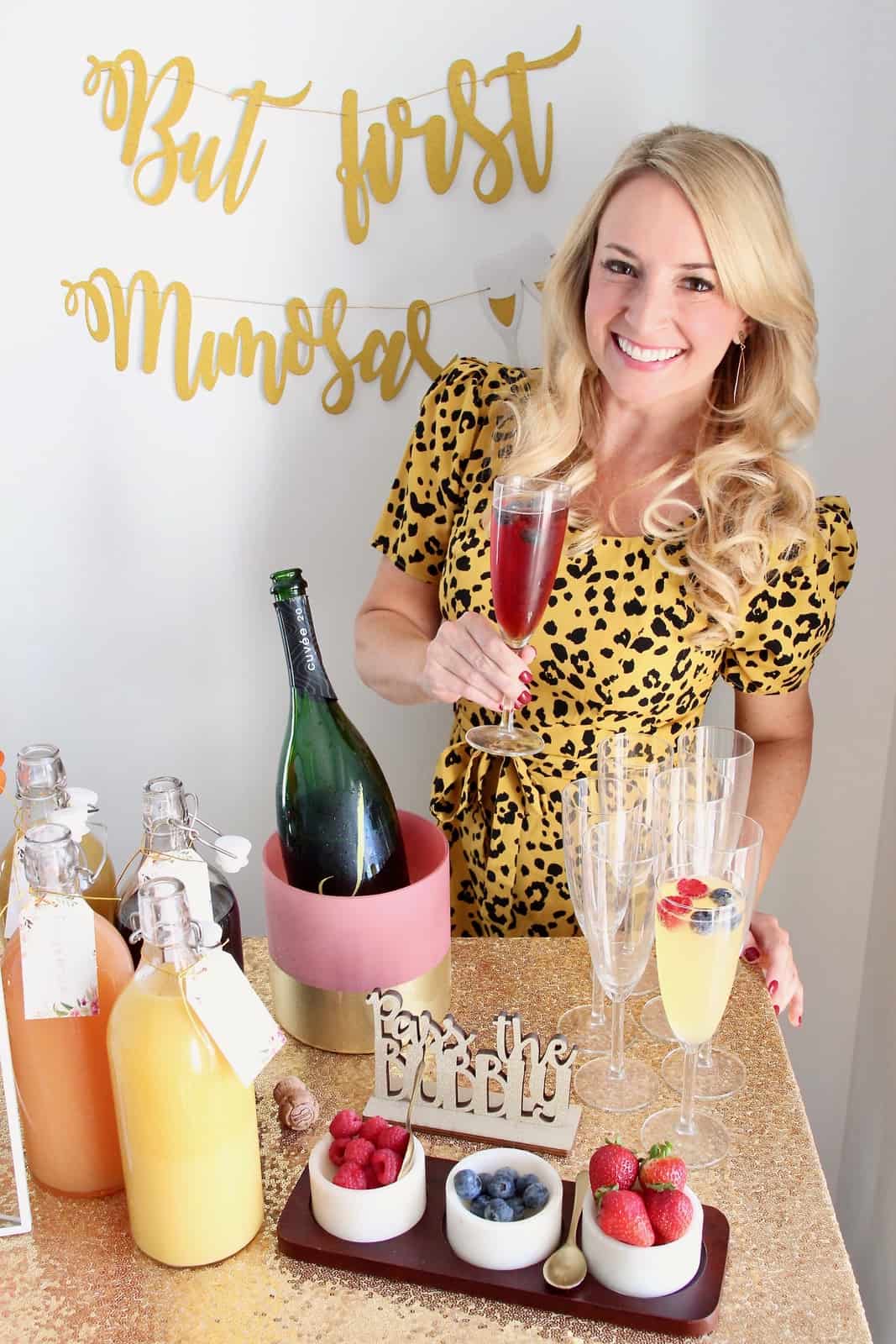 Woman holding mimosa standing behind mimosa bar