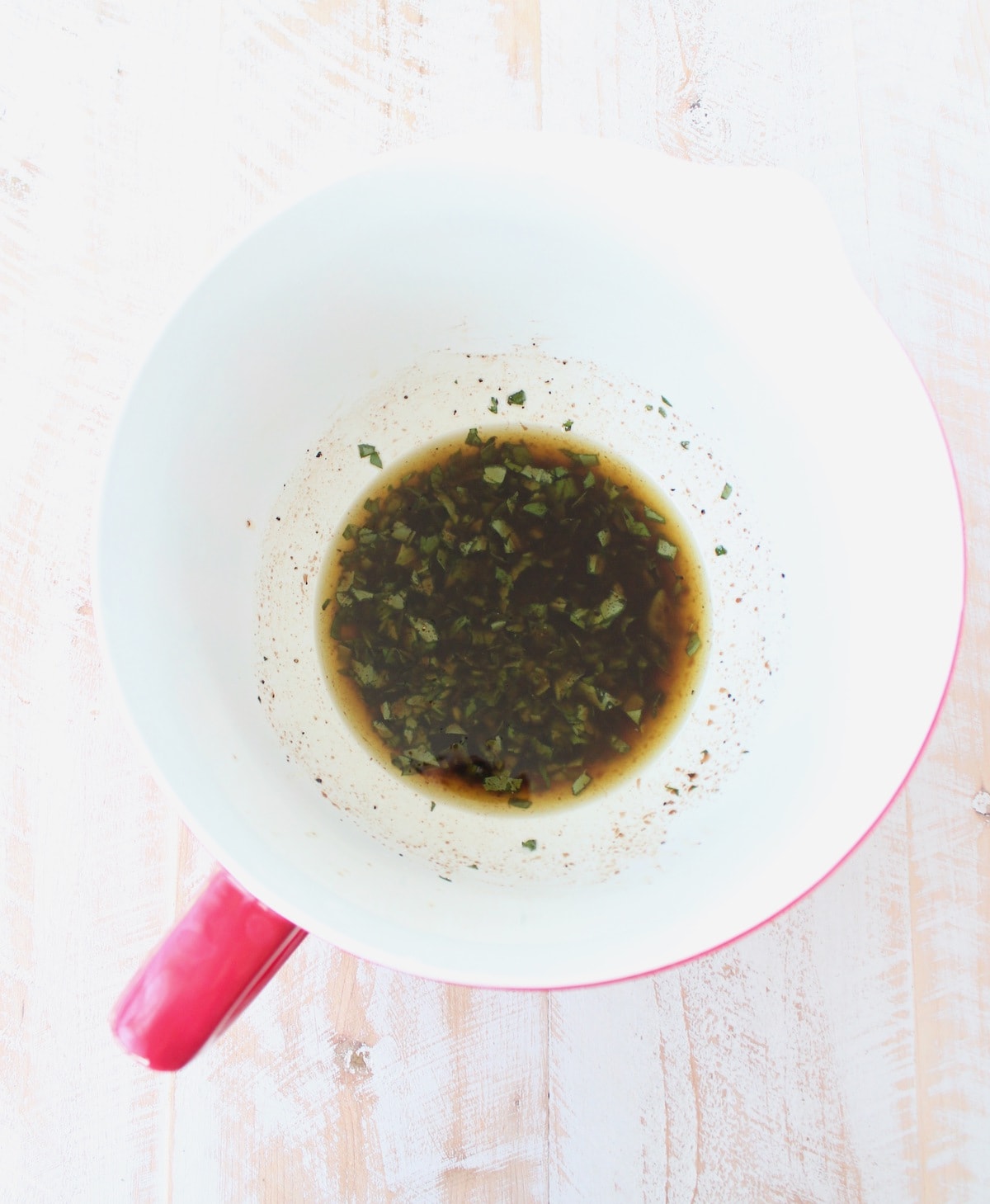 olive oil, basil, parsley, balsamic vinegar, lemon juice, salt and pepper in a white and red bowl. 