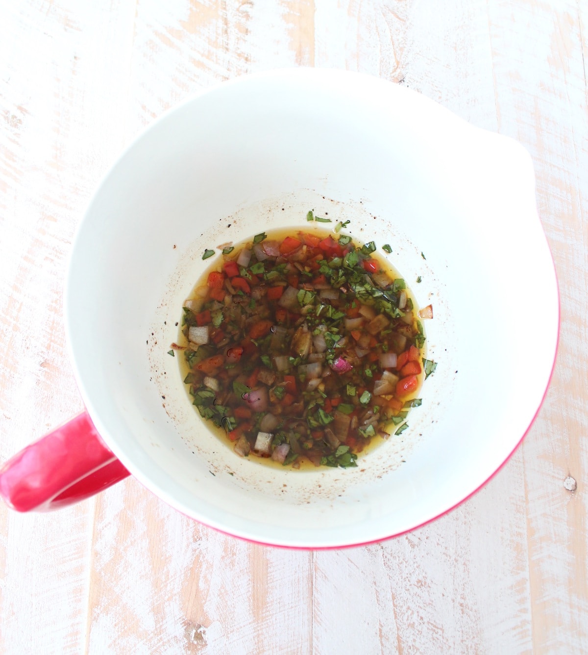 Onions, peppers, olive oil, basil, parsley, balsamic vinegar, lemon juice, salt and pepper in a white and red bowl. 