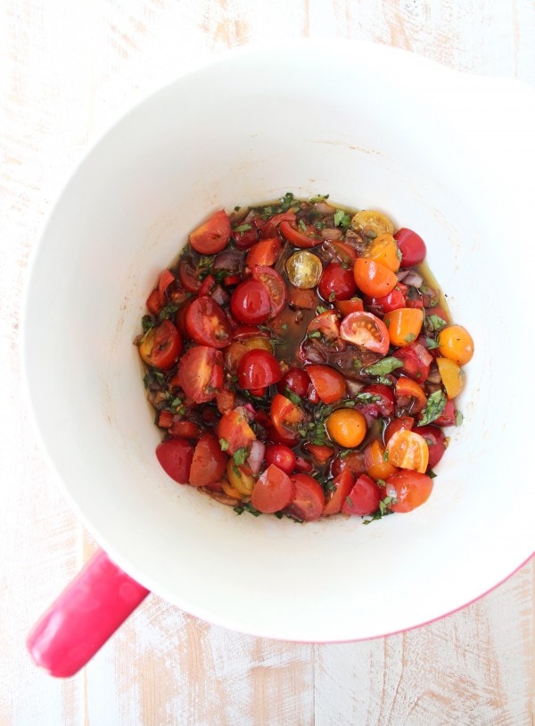 Tomatoes, onions, peppers, olive oil, basil, parsley, balsamic vinegar, lemon juice, salt and pepper in a white and red bowl. 