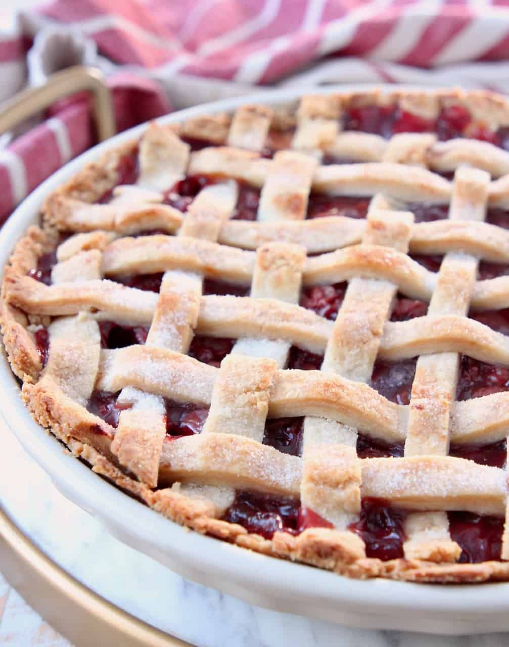 cherry pie with lattice crust in pie plate on marble serving tray