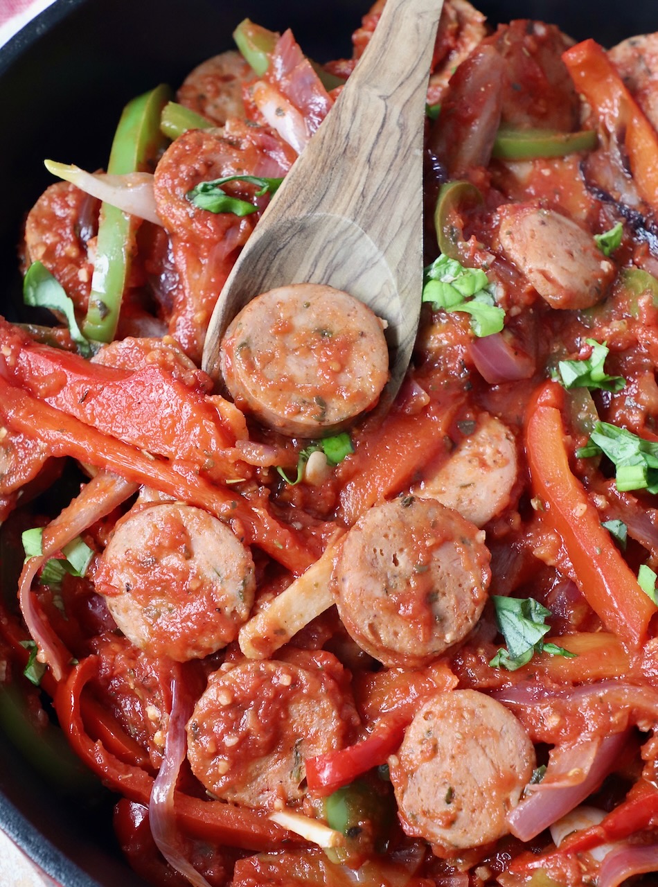 sliced sausage and peppers in skillet with wooden serving spoon