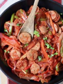 cooked sliced bell peppers and sausage in skillet with wooden spoon