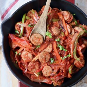 cooked sliced bell peppers and sausage in skillet with wooden spoon