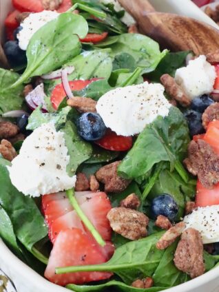 spinach salad in large bowl topped with berries, pecans and ricotta cheese
