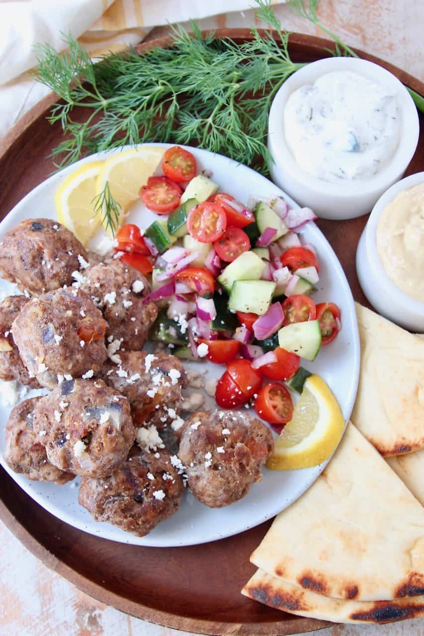 Greek meatballs on plate with tomato cucumber salad and slices of pita bread on the side