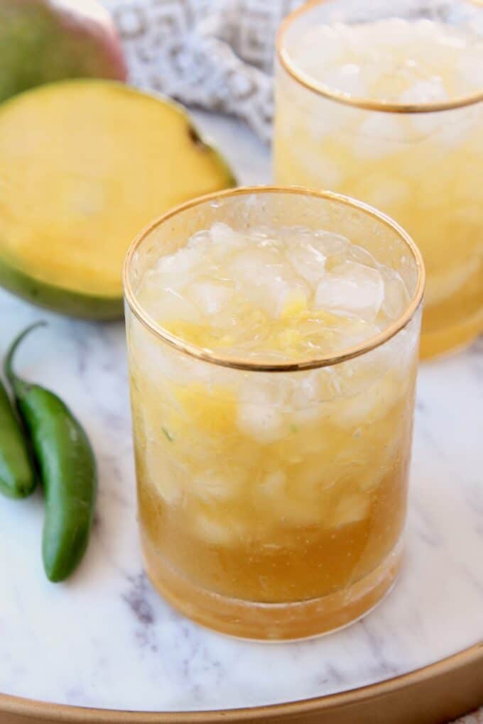 Mango margaritas in glasses on marble tray with fresh mango sliced open