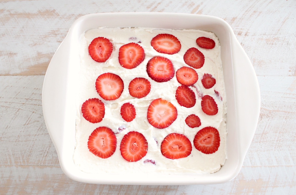 sliced strawberries on top of prepared cheesecake bars in square dish