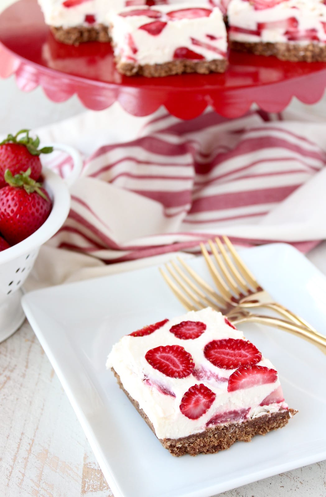 strawberry cheesecake bar with graham cracker crust on white plate with gold forks