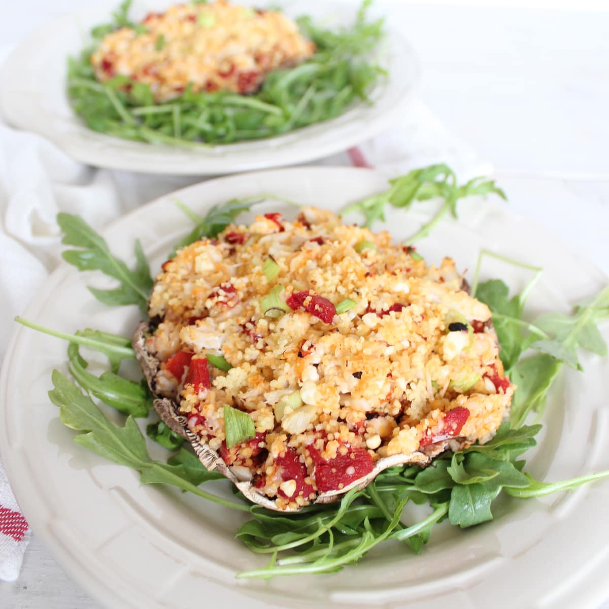 portobello mushroom stuffed with crab, couscous and vegetables on a bed of arugula on a plate