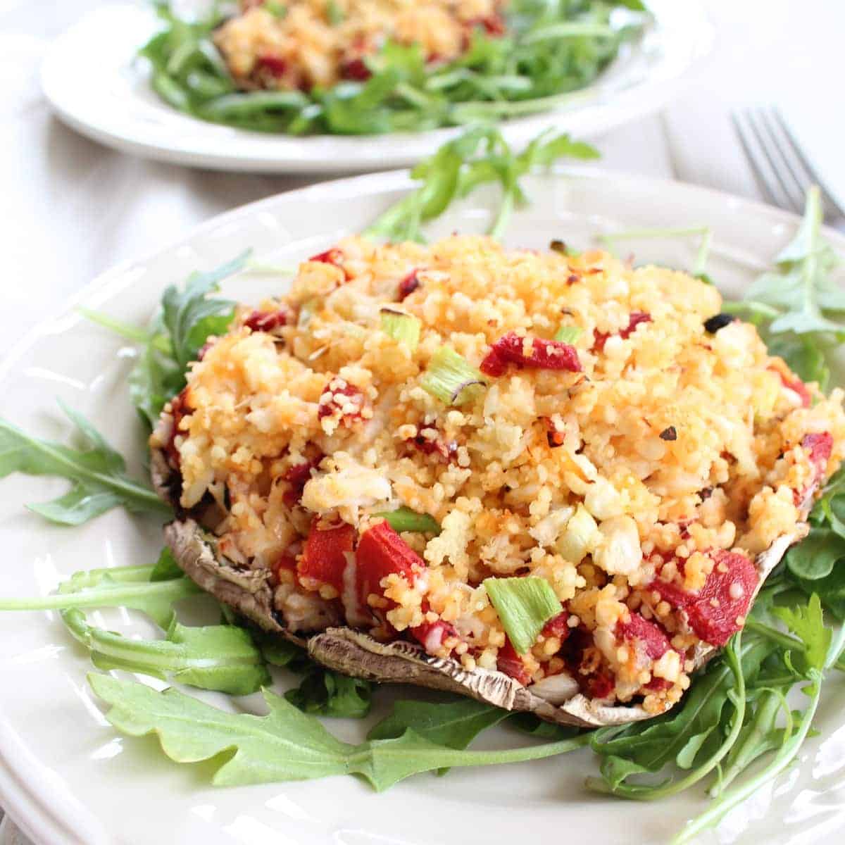 portobello mushroom stuffed with crab, couscous and vegetables on a bed of arugula on a plate