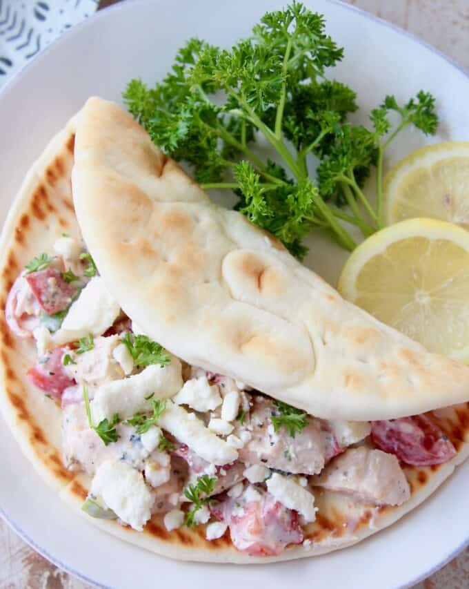 overhead image of chicken salad in pita bread on plate with lemon wedges and parsley
