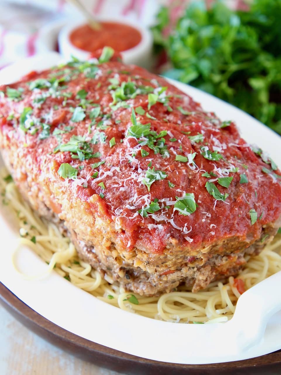 Italian meatloaf sitting on top of a bowl of spaghetti noodles, topped with fresh chopped parsley
