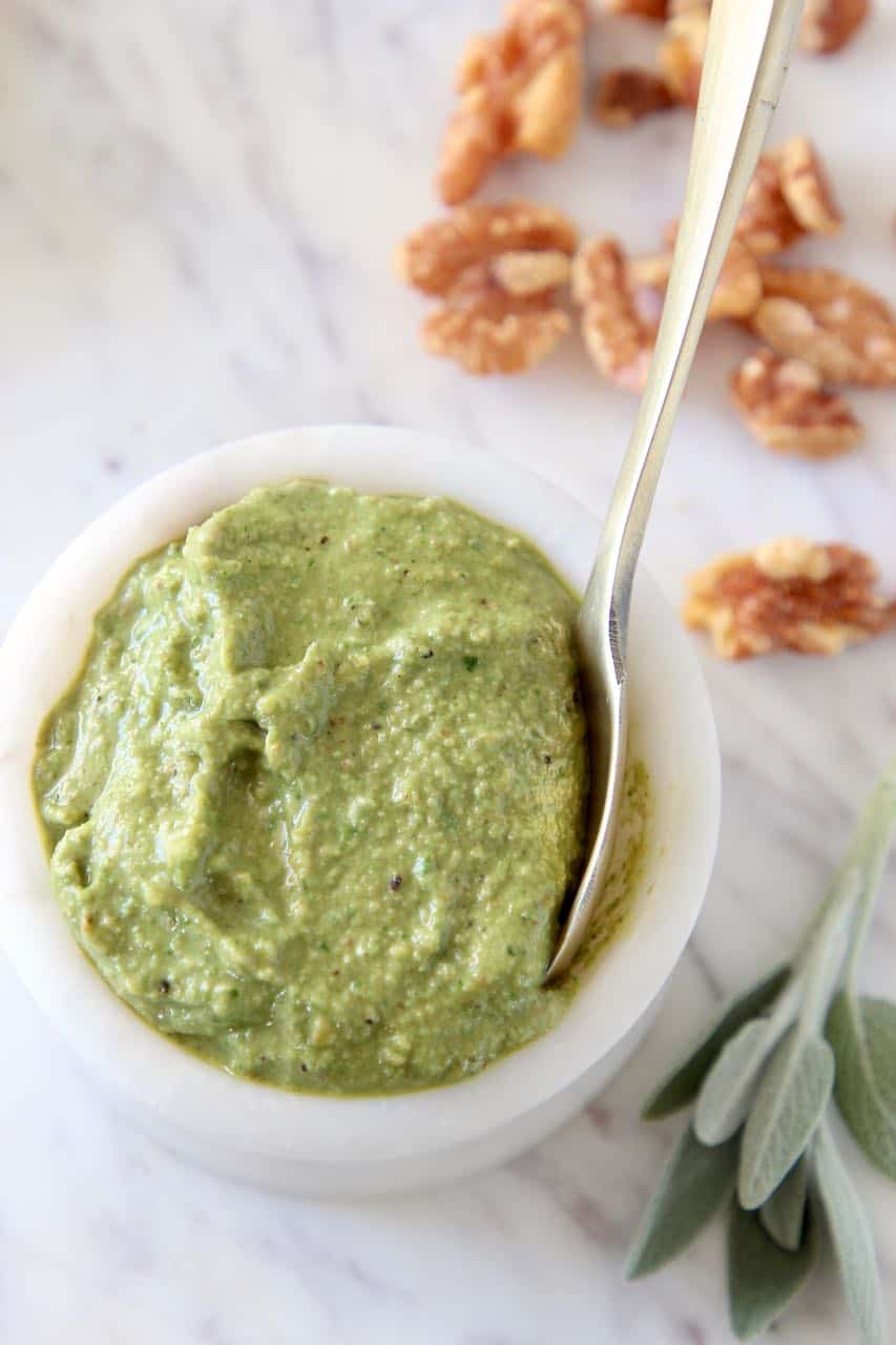 Sage pesto in white marble bowl with small gold spoon