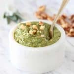 Sage pesto in marble white bowl with gold spoon, topped with chopped walnuts