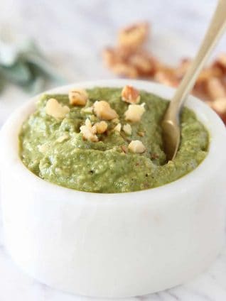 Sage pesto in marble white bowl with gold spoon, topped with chopped walnuts