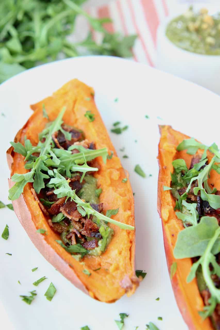 Loaded sweet potato skins with bacon and arugula on white plate