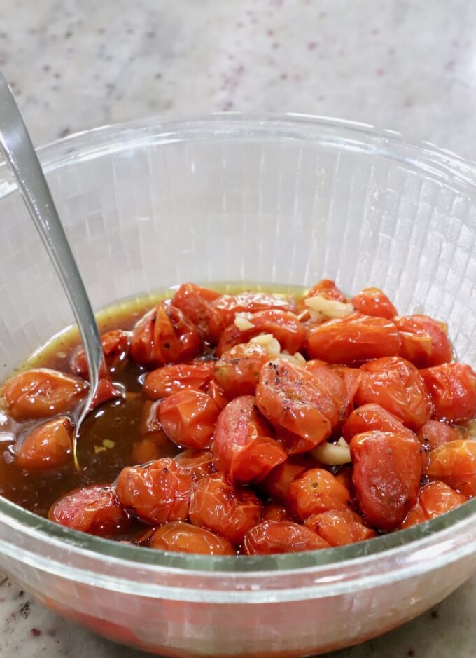 roasted cherry tomatoes with garlic and balsamic vinegar in a glass bowl with a spoon