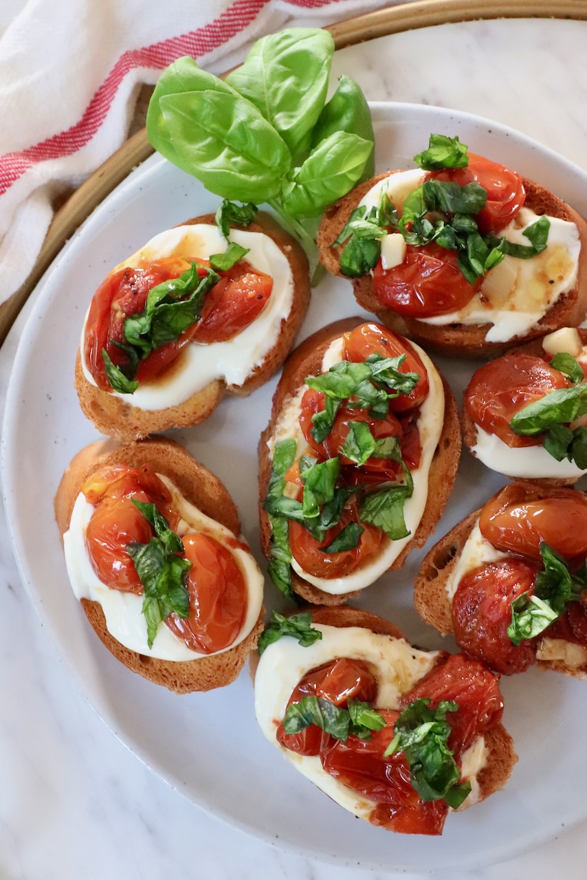 whipped ricotta and roasted tomato bruschetta on a plate with fresh basil leaves