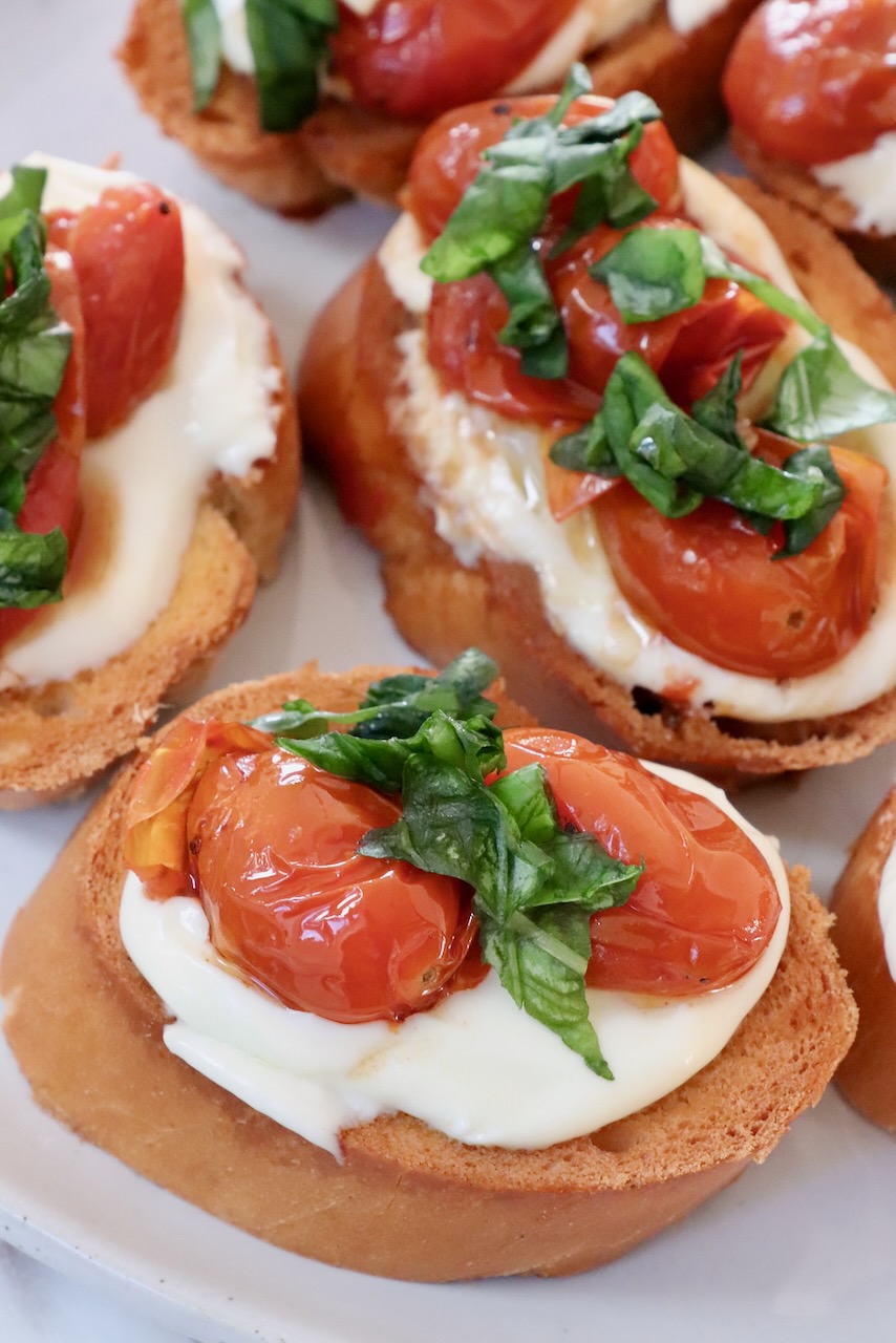 roasted tomatoes and whipped ricotta cheese on slices of baguette on a plate