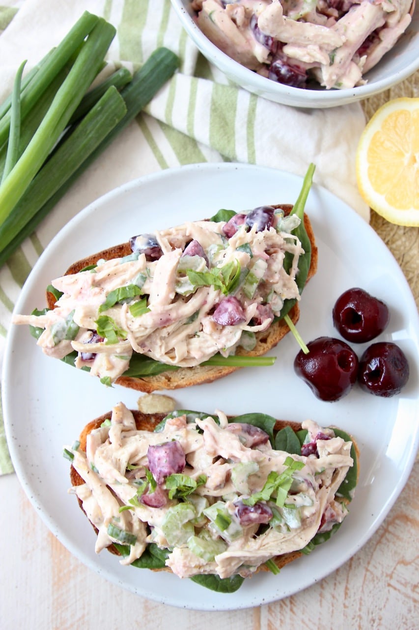 Overhead shot of open face chicken salad sandwiches on a white plate with cherries