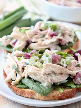 Chicken salad on toast with spinach and cherries on a white round plate