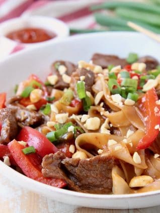 Kung pao beef, rice noodles, green onions and sliced red bell peppers in large white bowl