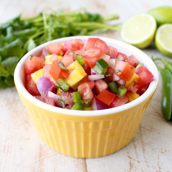 A yellow dish filled with diced mango, tomatoes, onions, and jalapeños.