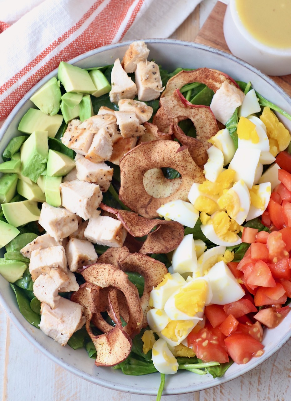 cobb salad in bowl topped with apple chips, eggs, tomatoes, chicken and avocado