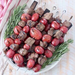 steak and potato kebabs stacked up on plate with rosemary sprigs