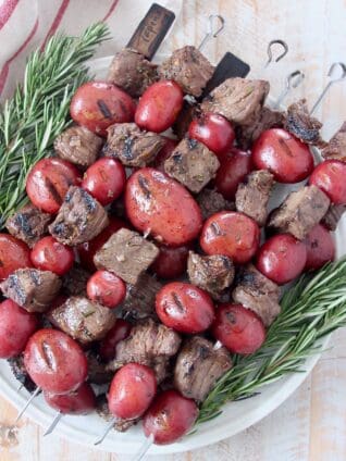 steak and potato kebabs stacked up on plate with rosemary sprigs