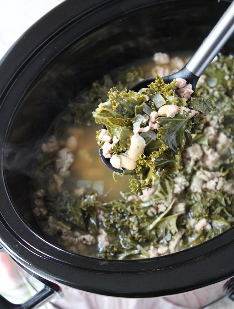 Turkey kale soup in spoon coming out of a crock pot full of soup