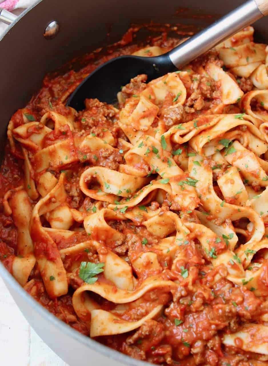 Pasta tossed in meat sauce in large pot with serving spoon in the pot