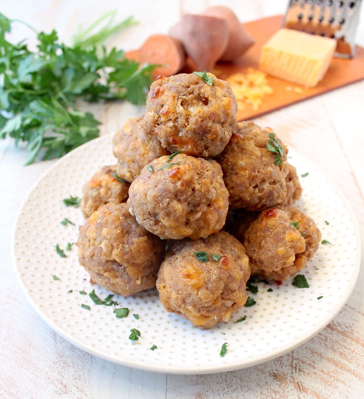 sweet potato sausage balls stacked on a white plate. 