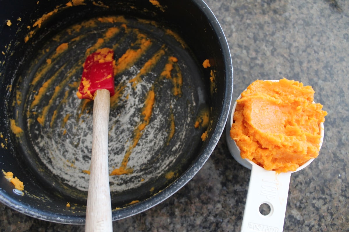 Mashed Sweet Potatoes in a white measuring cup next to an empty pot. 