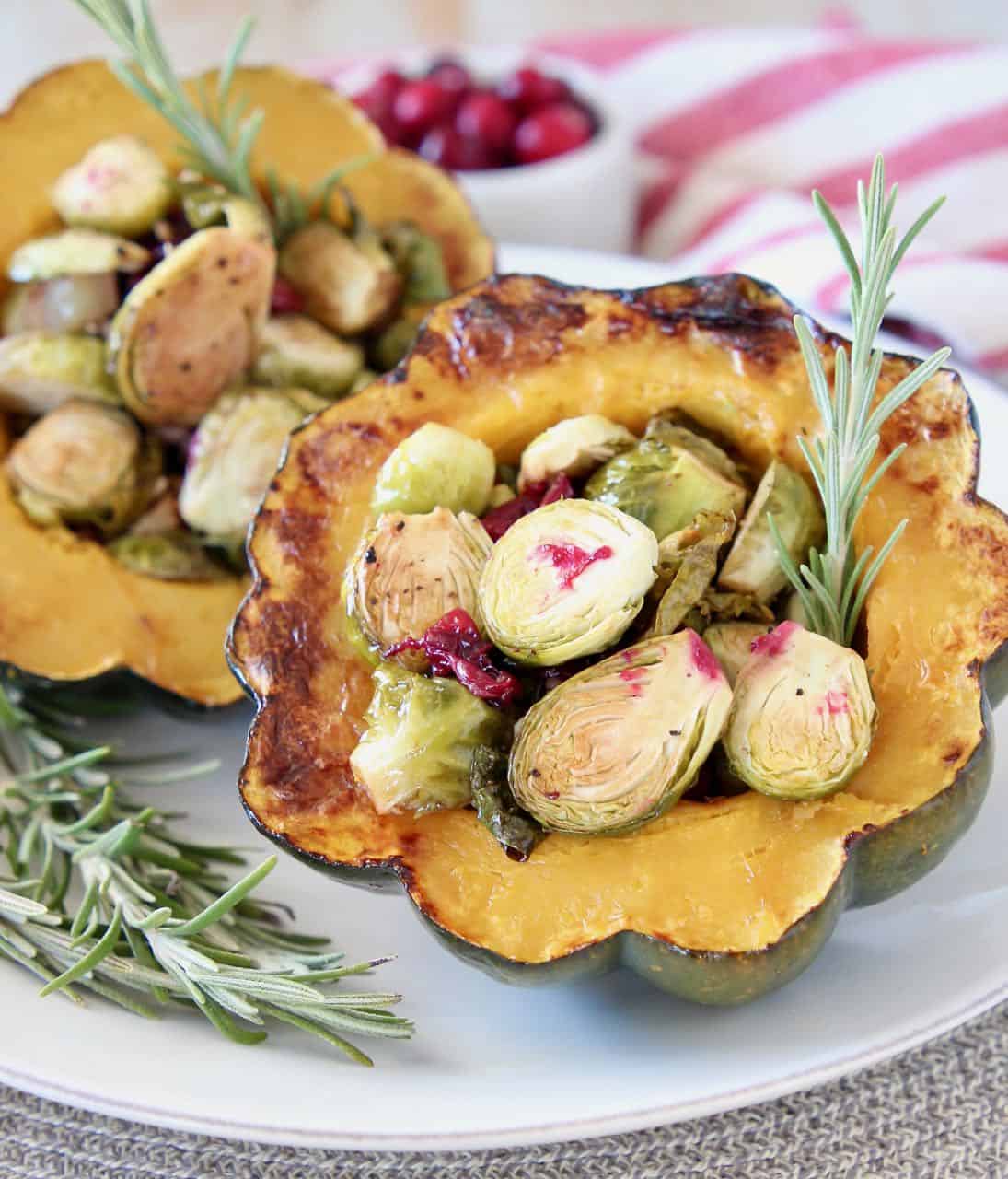 Stuffed acorn squash halves on plate filled with roasted brussels sprouts and cranberries