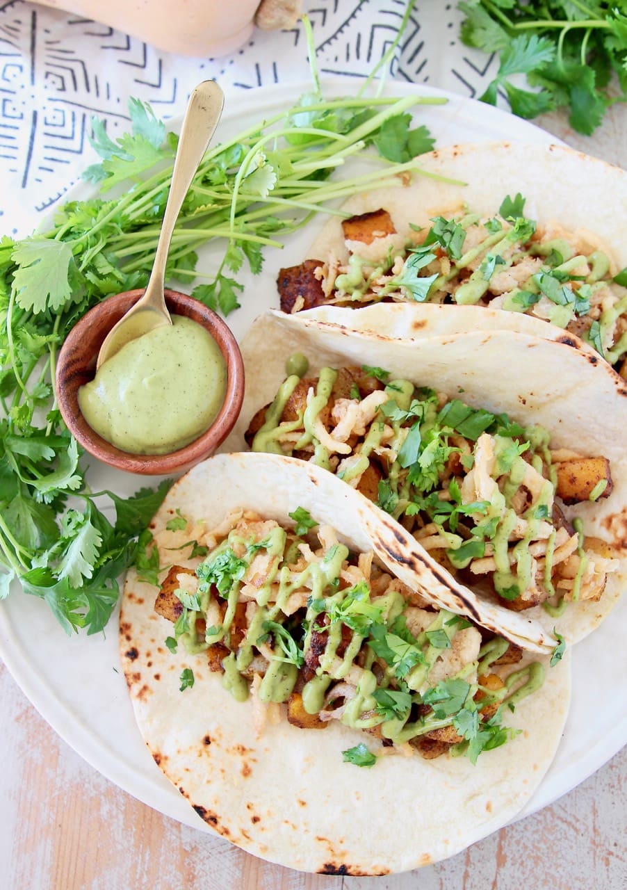 Butternut squash tacos topped with crispy onions, avocado cream sauce and fresh cilantro on plate