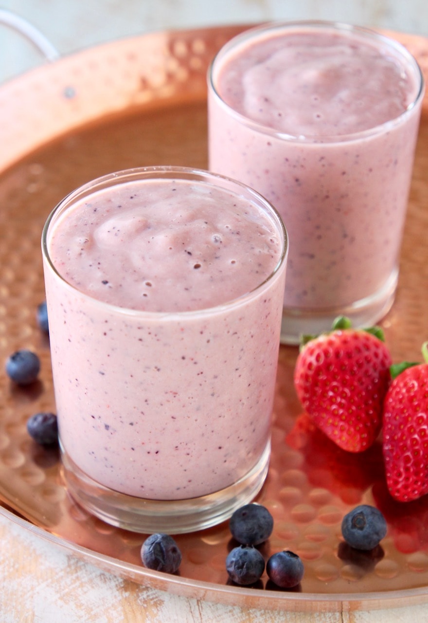 Heart healthy fruit smoothie in two glasses on copper tray with fresh strawberries and blueberries