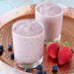 Fruit smoothie in glasses on copper tray with strawberries and blueberries