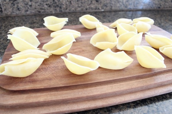 Cooked pasta shells on a wooden cutting board. 