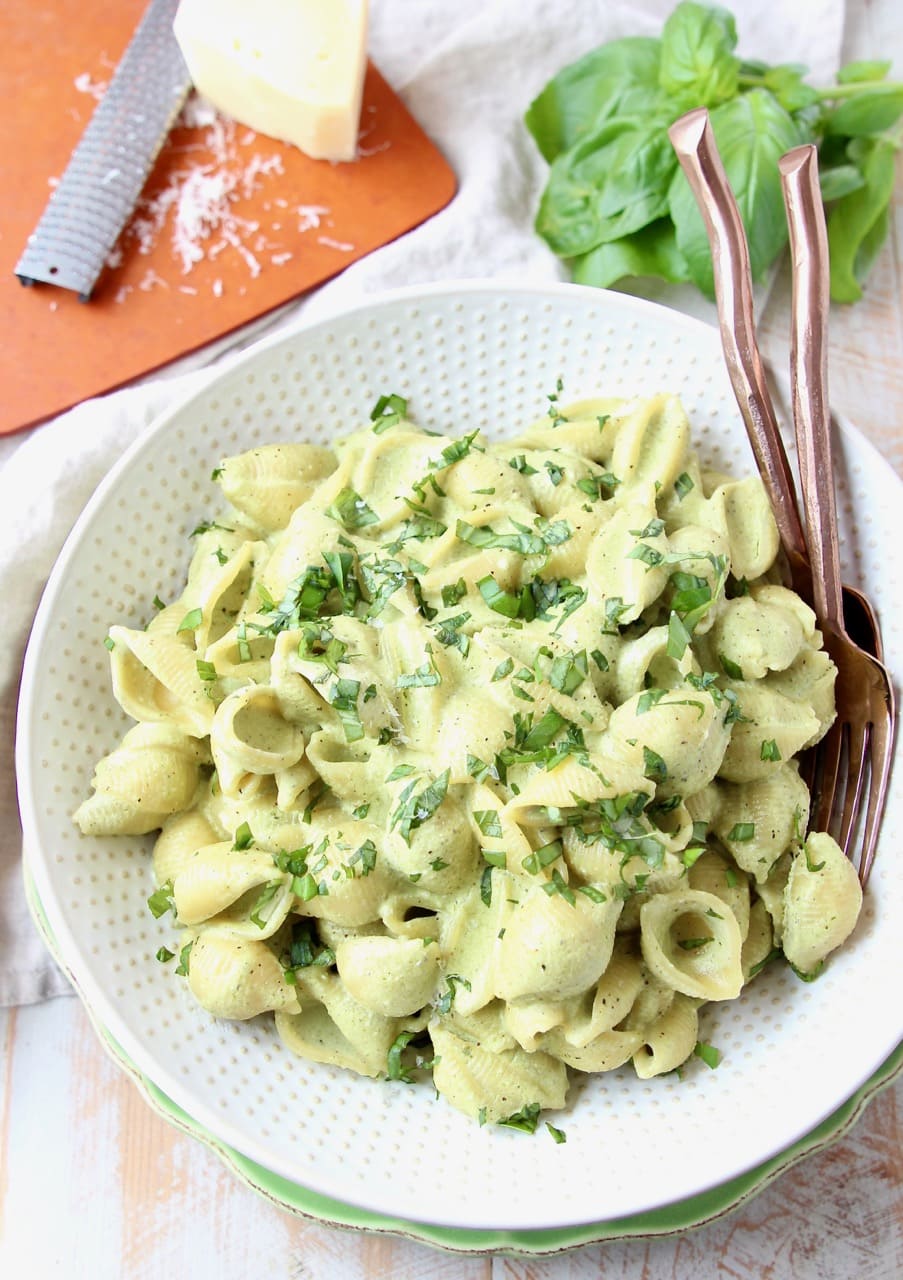 Cheesy pesto pasta shells in large white bowl with copper forks in the bowl